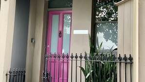 Un bâtiment avec une porte rose, un balcon orné de rampes en métal ouvragé et des plantes en pot.
