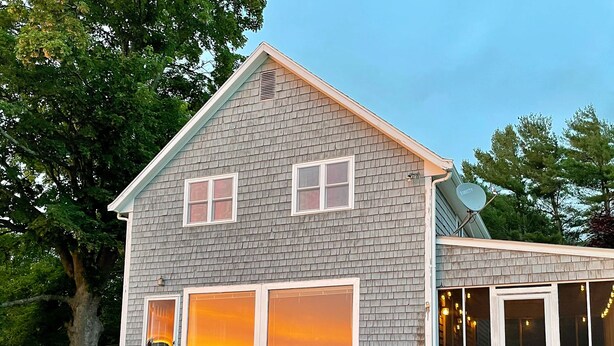 A two-story house with a stone foundation, large windows, and a stone staircase leading to the entrance. - Windsurfers Cove, shore front cottage (Tiverton)