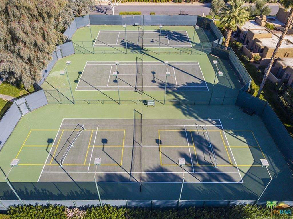 An aerial view of a tennis court complex with multiple courts, surrounded by greenery and residential buildings.