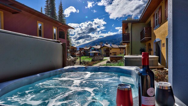 Ein Whirlpool mit einer Weinflasche und einem Glas, umgeben von Gebäuden und Blick auf einen Berg.