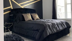 A modern bedroom with a black bed, geometric wall design, and a chandelier.