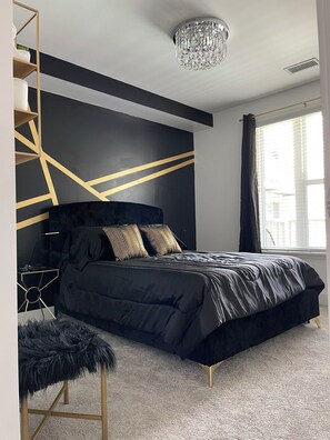 Une chambre à coucher moderne avec un lit noir, un motif géométrique sur le mur et un lustre.