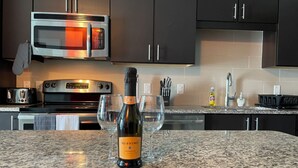 A kitchen with dark cabinets, a stainless steel microwave, a toaster, and a bottle of wine on the counter.