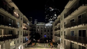 A multi-story hotel with balconies, a courtyard with a pool, and a view of a tall building in the background.