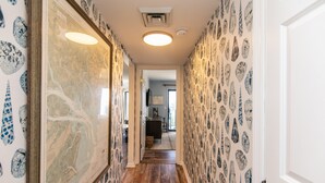 Un pasillo con papel tapiz estampado y suelo de madera, que conduce a una habitación con un sofá oscuro y una mesa.