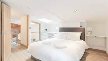 A modern hotel room with a large bed, a wooden door, a white wall, and a skylight.