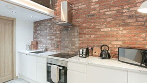 A modern kitchen with white cabinetry, a brick accent wall, a built-in oven, a kettle, and a microwave. - LN Collection - Grassmarket (Edinburgh)