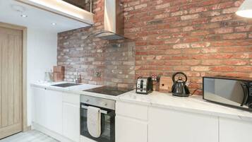 A modern kitchen with white cabinetry, a brick accent wall, a built-in oven, a kettle, and a microwave.