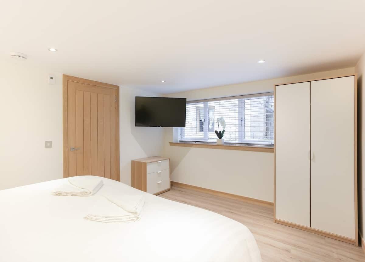 A bedroom with a bed, a TV mounted on the wall, a wardrobe, and a window with blinds.