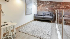 A modern living room with a grey sofa, a small white table with a remote control, a grey rug, and a brick wall accent. - LN Collection - Grassmarket (Edinburgh)