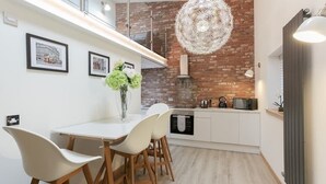 A modern kitchen with white cabinetry, a brick accent wall, and a hanging light fixture. - LN Collection - Grassmarket (Edinburgh)