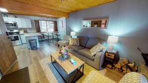 A modern kitchen with white cabinets, a dining area with a table and chairs, a living room with a sofa and a coffee table, and a fireplace with wood logs. - Fireplace | WiFi | Close to Lifts | Windchimes 212 (Angel Fire)