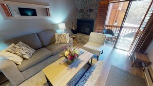 A cozy living room with a sofa, armchair, and coffee table, a fireplace, and a balcony with a view. - Fireplace | WiFi | Close to Lifts | Windchimes 212 (Angel Fire)