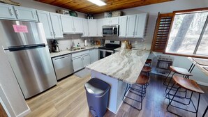 A compact kitchen with white cabinets, a stainless steel refrigerator, a microwave, and a granite countertop island with bar stools. - Fireplace | WiFi | Close to Lifts | Windchimes 212 (Angel Fire)