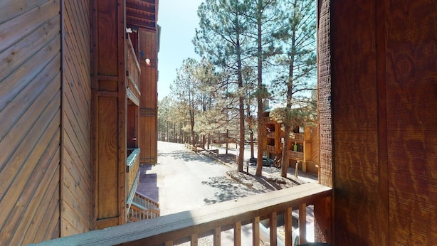 A wooden cabin with a balcony overlooking a snowy path and pine trees. - Fireplace | WiFi | Close to Lifts | Windchimes 212 (Angel Fire)