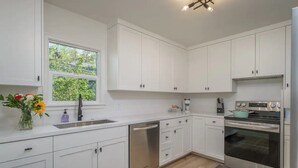 A modern kitchen with white cabinets, stainless steel appliances, a window with a view of greenery, and a vase with flowers on the counter. - A Modern Minimalist's Dream- near DT, UNR & FWY (Reno)
