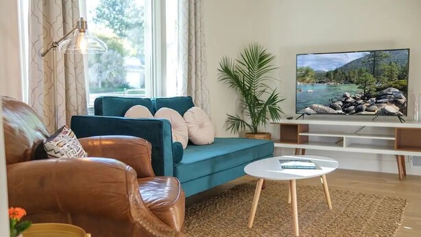A living room with a sofa, a coffee table, and a TV displaying a scenic landscape. - A Modern Minimalist's Dream- near DT, UNR & FWY (Reno)