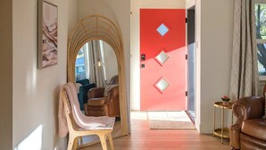 A room with a wooden floor, a red door with diamond-shaped cutouts, a brown leather sofa, a wooden chair, and a small table with a plant. - A Modern Minimalist's Dream- near DT, UNR & FWY (Reno)