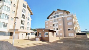 A multi-story residential building with balconies, a small kiosk, and a paved courtyard. - Puerto Romano II 88 by homeprive (Denia)
