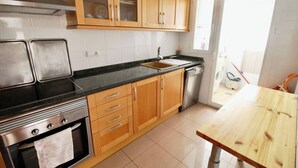 A kitchen with wooden cabinets, a stainless steel oven, a sink, and a wooden table. - Puerto Romano II 88 by homeprive (Denia)