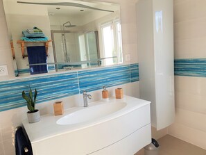 A modern bathroom with a glass-enclosed shower, a white sink with a wooden countertop, and a mirror above the sink. - Villa classified 4 stars with air conditioning, heated swimming pool.  (Nézignan-l'Évêque)