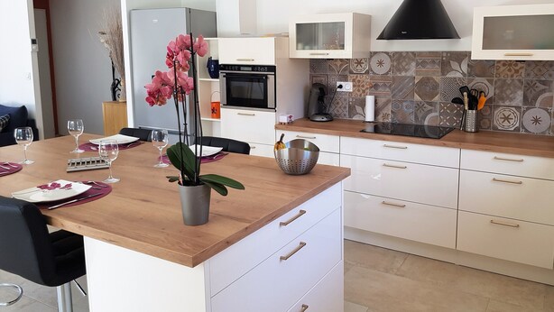 Una cocina moderna con armarios blancos, encimera de madera, campana extractora negra y salpicadero de azulejos.