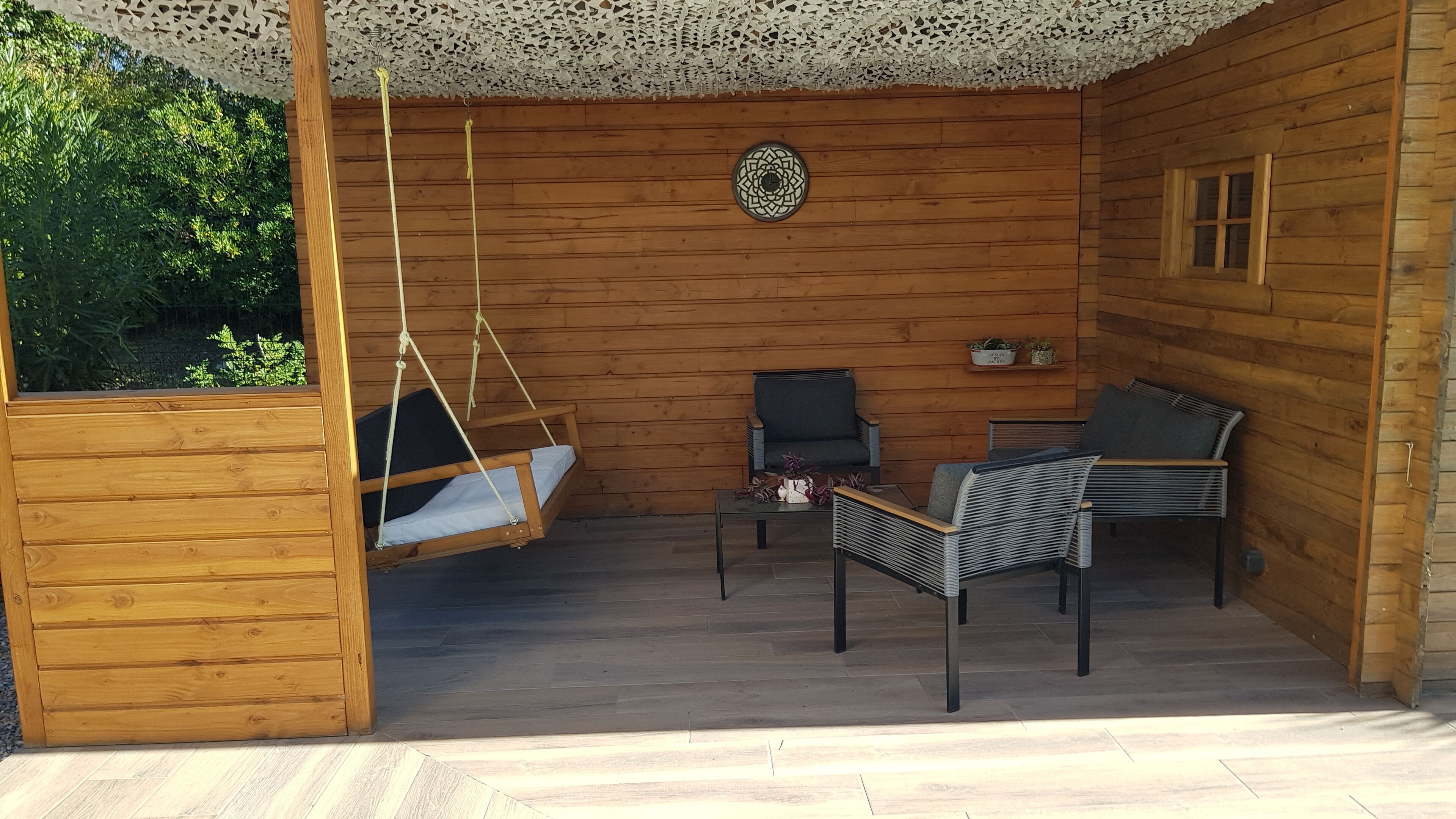 Eine Holzhütte mit einer Hängematte, einem gepolsterten Sessel, einem kleinen Tisch und einer Wanddekoration.
