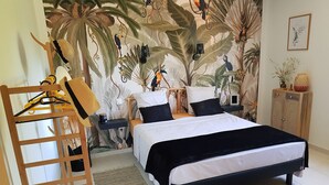 Un dormitorio con cama, una escalera de madera, una mesita de noche, un estante y una pared con un mural tropical.