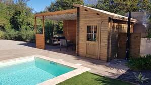Una cabaña de madera con piscina, un conjunto de columpios y un área de estar cubierta.