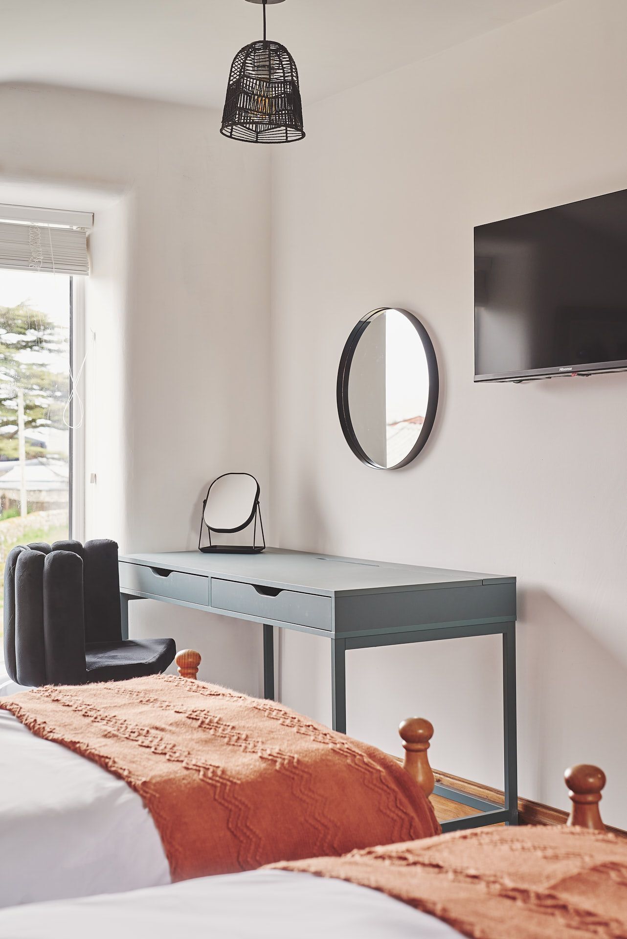 A bedroom with a bed, a desk, a chair, a TV, and a window.