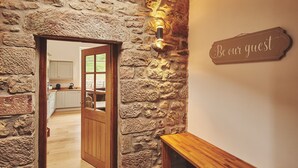 A stone wall with a wooden door leading to a kitchen. A sign on the wall reads "Be our guest." - Plum Cottage -  Luxury Cottages (Appleby)