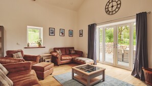 A spacious living room with leather sofas, a glass coffee table, and a large sliding glass door leading to an outdoor area. - Plum Cottage -  Luxury Cottages (Appleby)