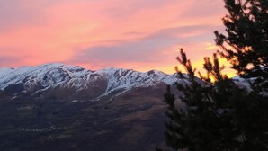 Een bergachtig landschap met besneeuwde toppen en een zonsonderganglucht.