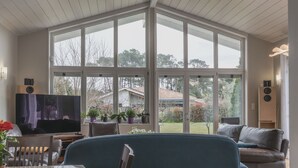 Amplia sala de estar con ventanas grandes, televisor, sofá y comedor con mesa y sillas.