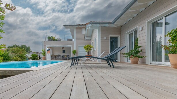 Una casa moderna con terraza de madera, piscina y sillas de descanso.