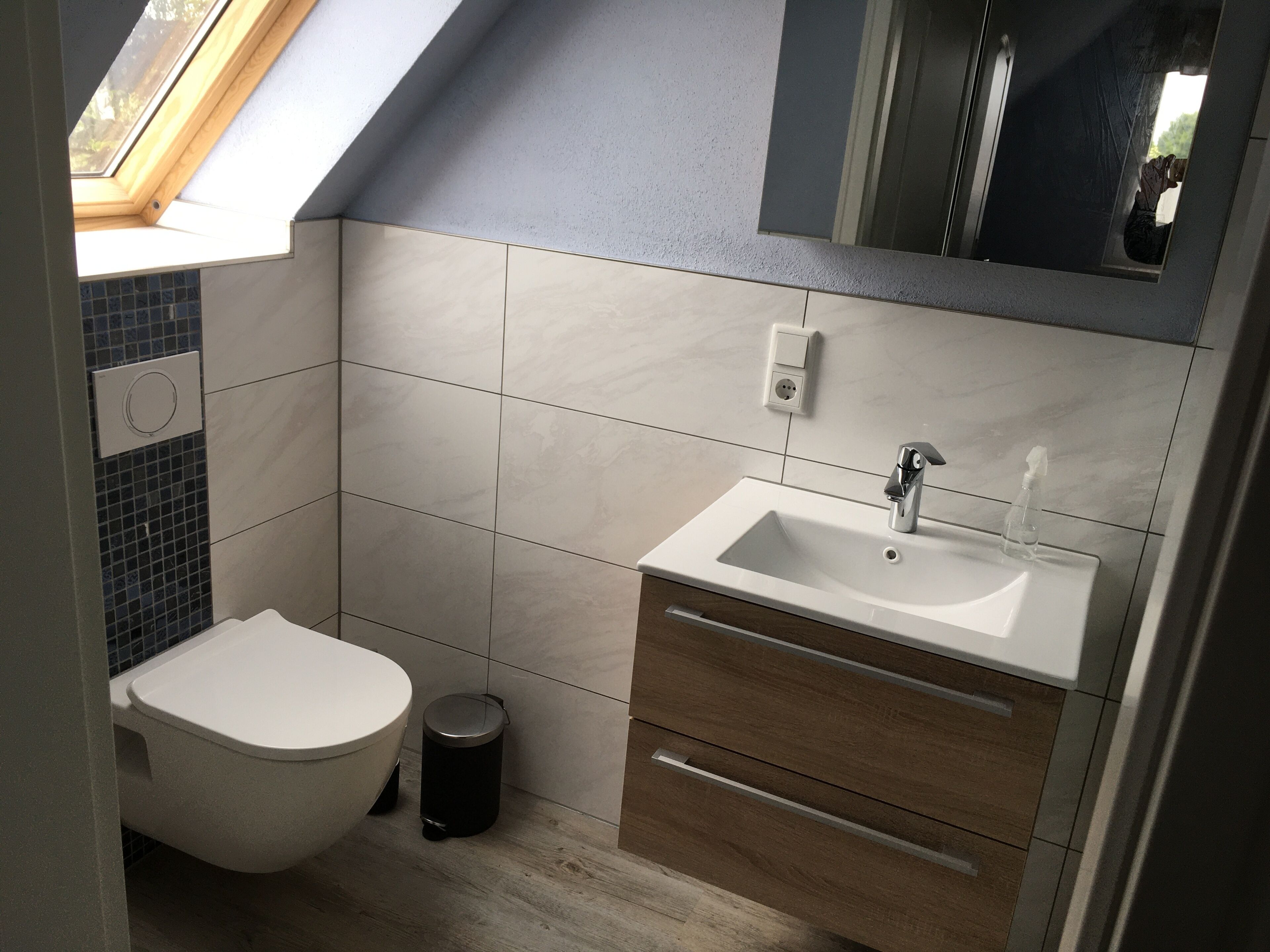 A modern bathroom with a skylight, a white sink, and a wooden vanity.