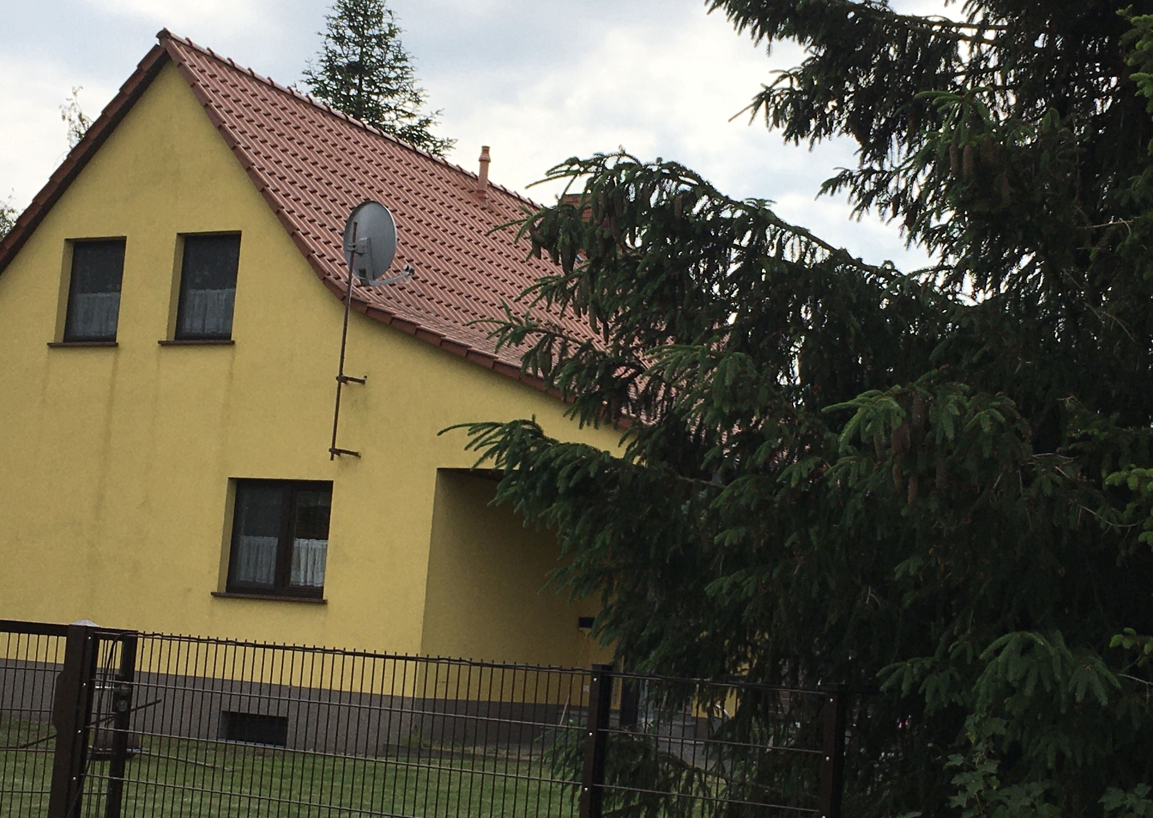 A yellow building with a red-tiled roof, a satellite dish, and a fenced yard.
