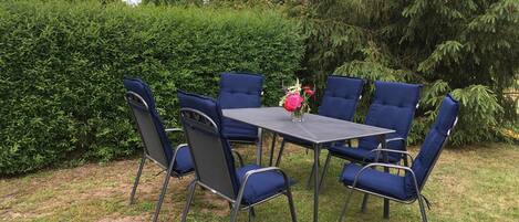 Une terrasse avec une table et des chaises, entourée de verdure.