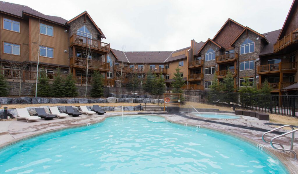 A hotel with a swimming pool, multiple balconies, and a stone facade.