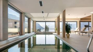 A modern indoor swimming pool with clear glass walls, large windows, and a view of mountains.
