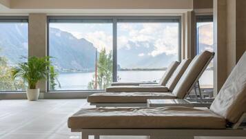 A modern lounge area with large windows offering a view of a lake and mountains.