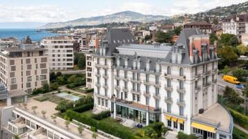 A multi-story hotel with a classic architectural style, featuring a central courtyard and a view of the sea.