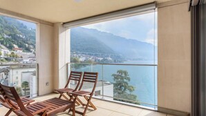 Een balkon met houten stoelen en een tafel, met uitzicht op een meer en bergen.