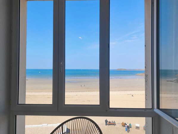 A window with a view of a beach, a chair, and a group of people.