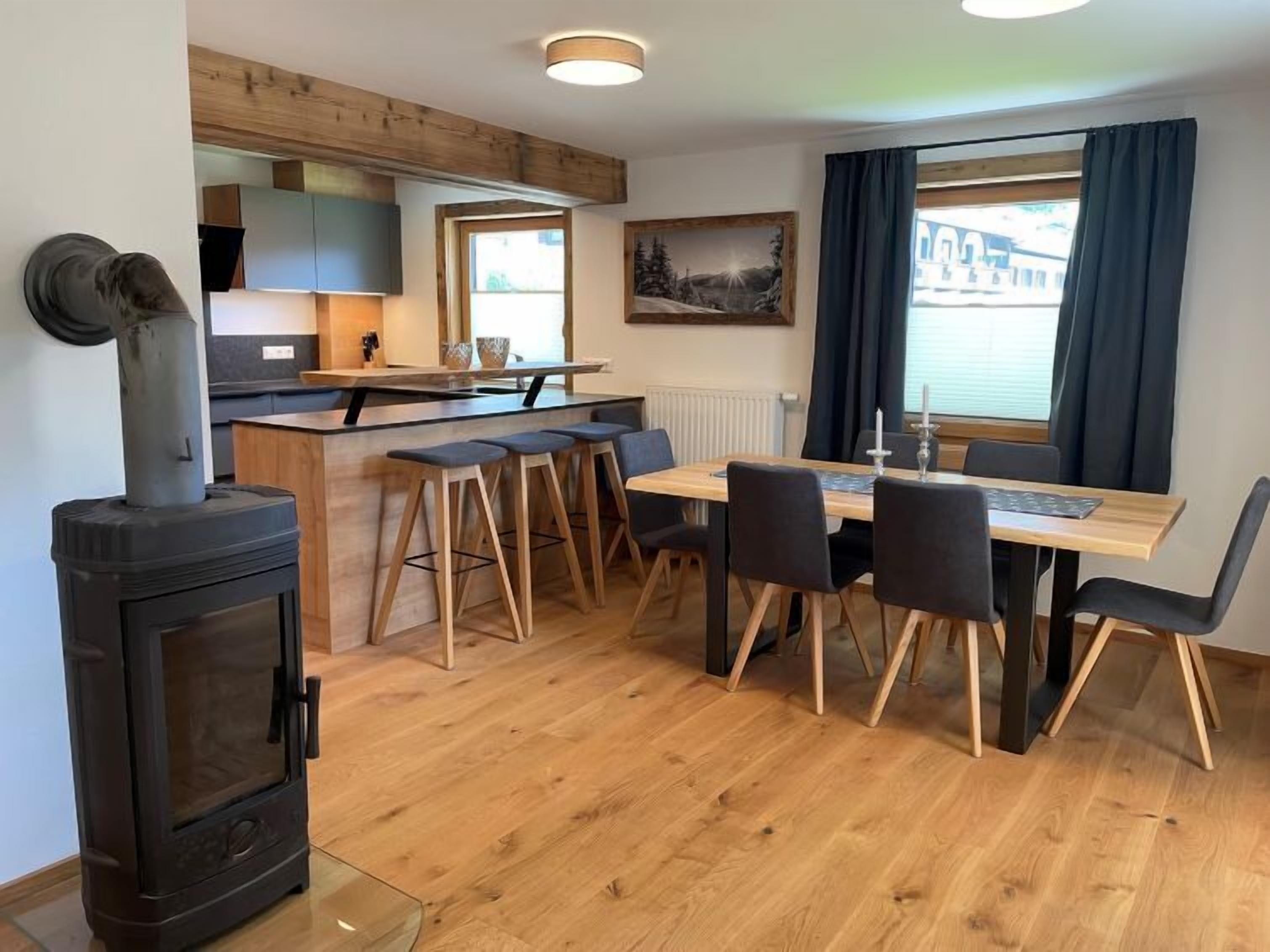 Une cuisine chaleureuse avec un poêle à bois, un coin repas avec une table et des chaises, et une vue magnifique grâce à de grandes fenêtres.