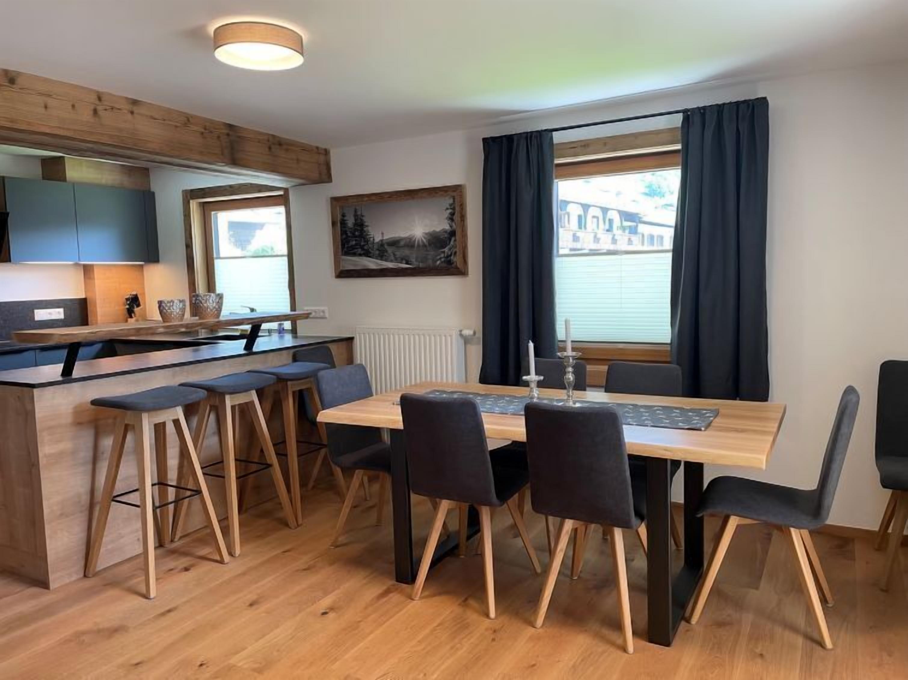 Une cuisine moderne agrémentée de touches de bois, un coin repas avec une table et des chaises, et une grande fenêtre avec des rideaux.