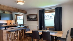 Une cuisine moderne agrémentée de touches de bois, un coin repas avec une table et des chaises, et une grande fenêtre avec des rideaux.