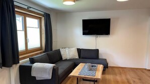 Un salon moderne avec un canapé d’angle, une table basse en bois et un téléviseur à écran plat fixé au mur.