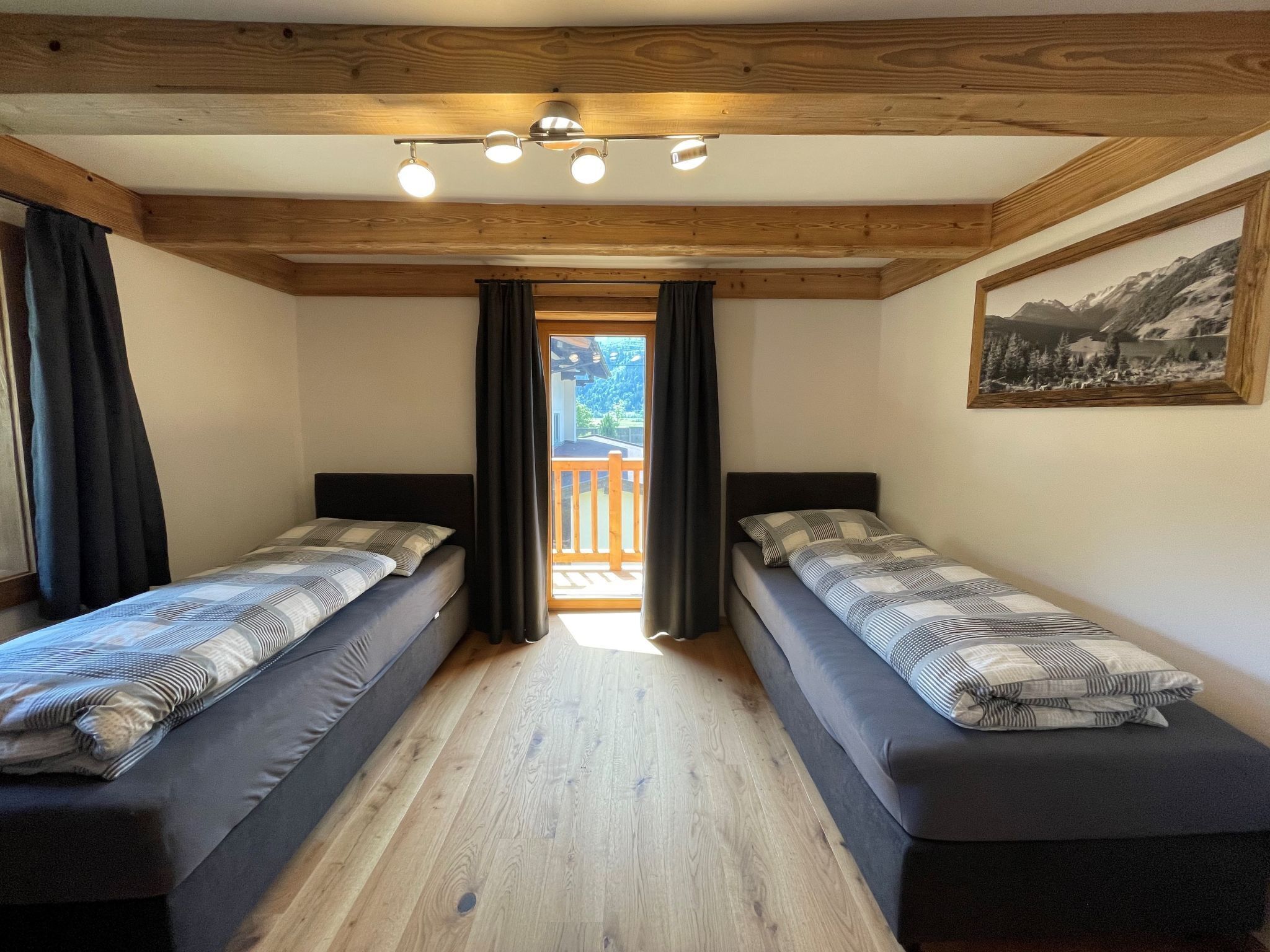 A room with two beds, wooden beams on the ceiling, a painting on the wall, and a balcony with a view.