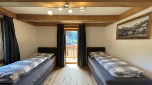 Une chambre avec deux lits, des poutres en bois au plafond, un tableau au mur et un balcon avec vue.